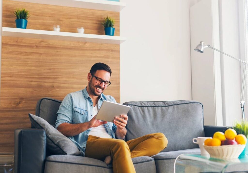 Smiling young man relaxing and using tablet on couch